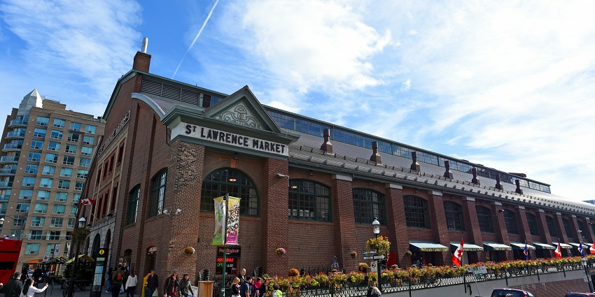 A distant side view of St. Lawrence Market outside which there are several cars parked.