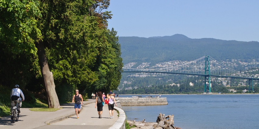 A distant view of Lions Gate Bridge is showcased along with people on the seawall