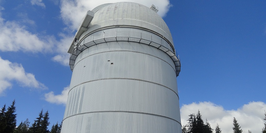 Rozhen observatory with a white building and a telescope behind the green trees