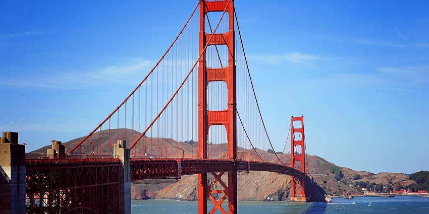 A large bridge spanning across a water reservoir with a mountain range in the backdrop