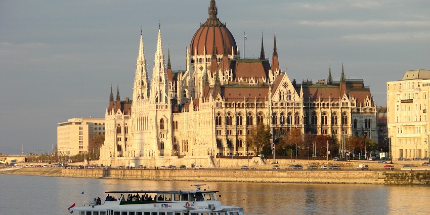 A cruise ship on the Danube River with the parliament building illuminated by sunlight