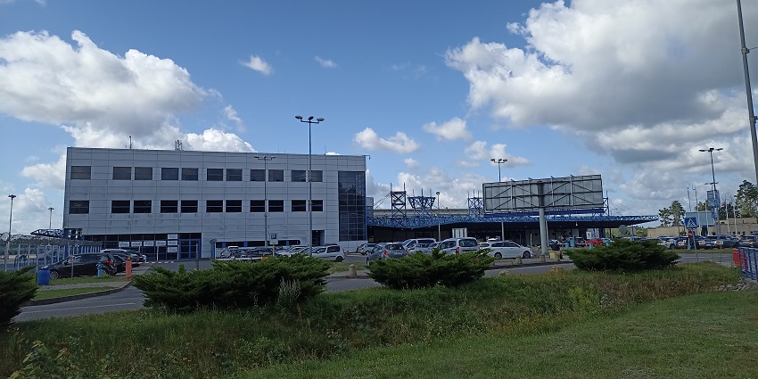 Szczecin-Goleniów Airport building from a parking lot with cars parked and billboards