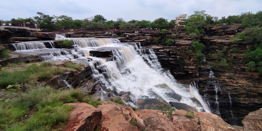 Scenic view of Tanda Falls surrounded by lush greenery and rocky cliffs.