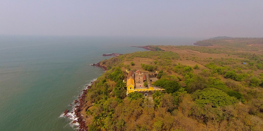 Aerial view of Terekhol Fort beside the sea, surrounded by lush greenery