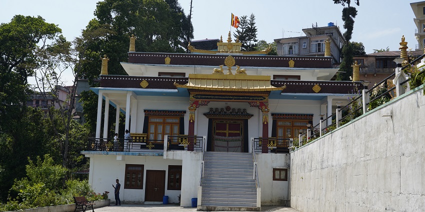 A picture of the Tharpa Choling Monastery, situated on a hill with prayer flags.