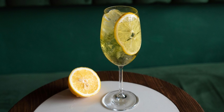 A picture of a glass of lemonde served with a a piece of lemon and on the side