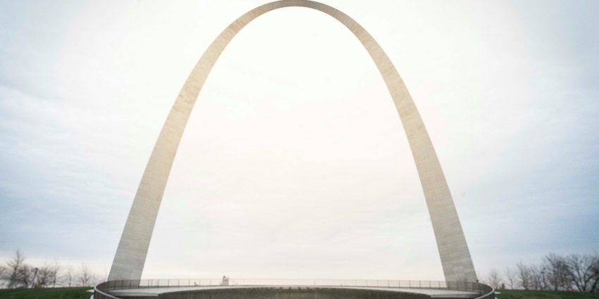 Distant view of the Gateway Arch with green grass in front and barren trees on the side