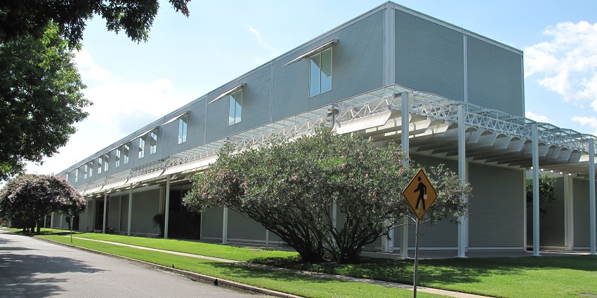 The Menil collection area and road with a modern building, signboard, and green trees