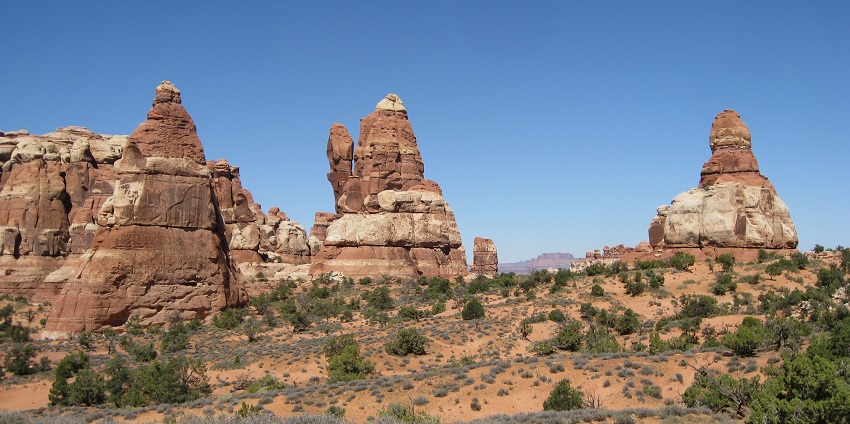 A vast desert landscape with red rock formations and sparse vegetation under a bright blue sky.