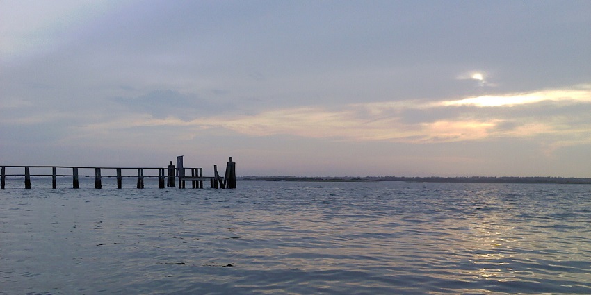 A pleasant view of Topsail Island’s sound side with calm water, marshland, and distant trees.