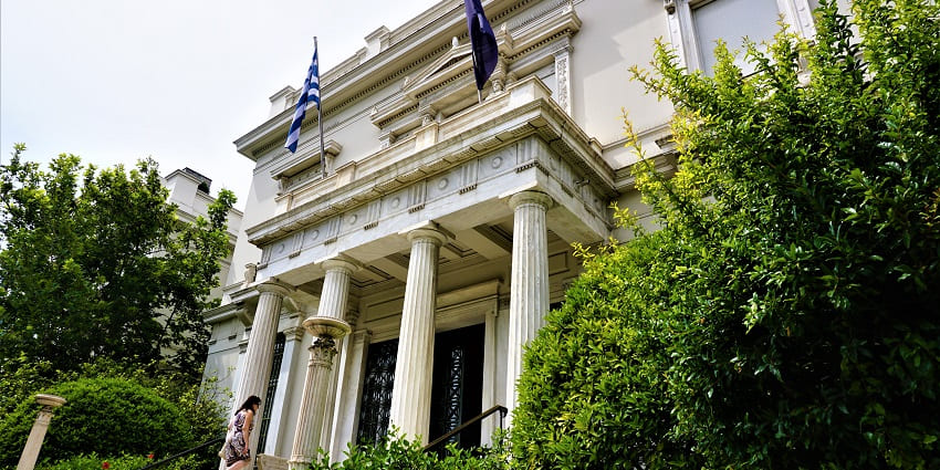 Benaki Museum with a Greek flag and a person climbing up the stairs to the entrance gate