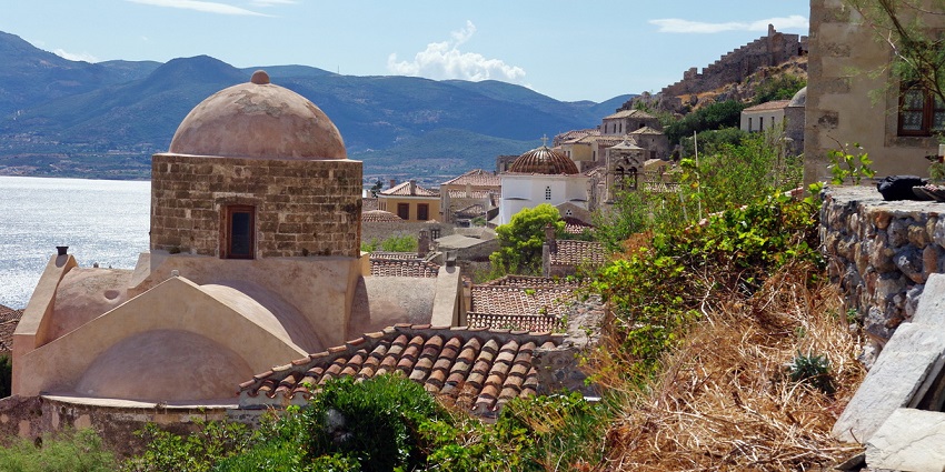 Monemvasia castle town with old-style buildings, a coastline and visible mountains.