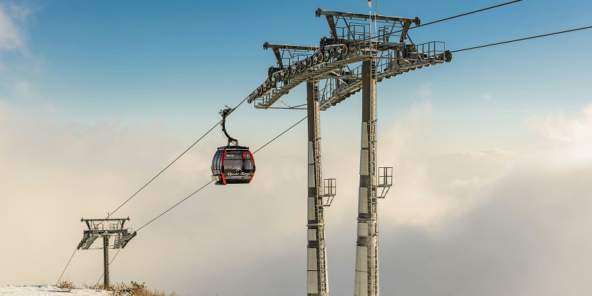 A cable car with a man standing inside it featuring all wooden structure and glass windows