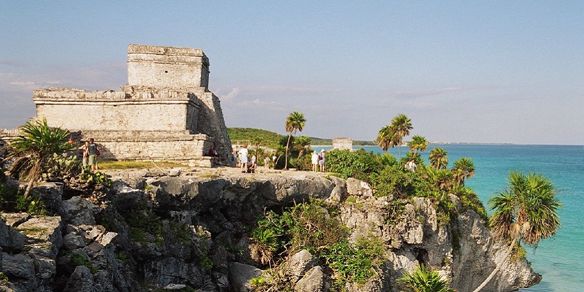 A distant view of a ruin that is situated on the top of a cliff overlooking the blue ocean