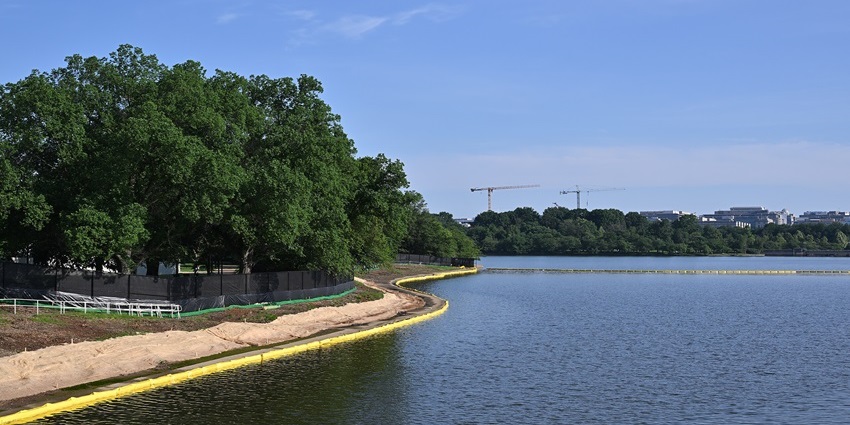 A large clean deep blue water body surrounded by trees and a seawall and ground on one side
