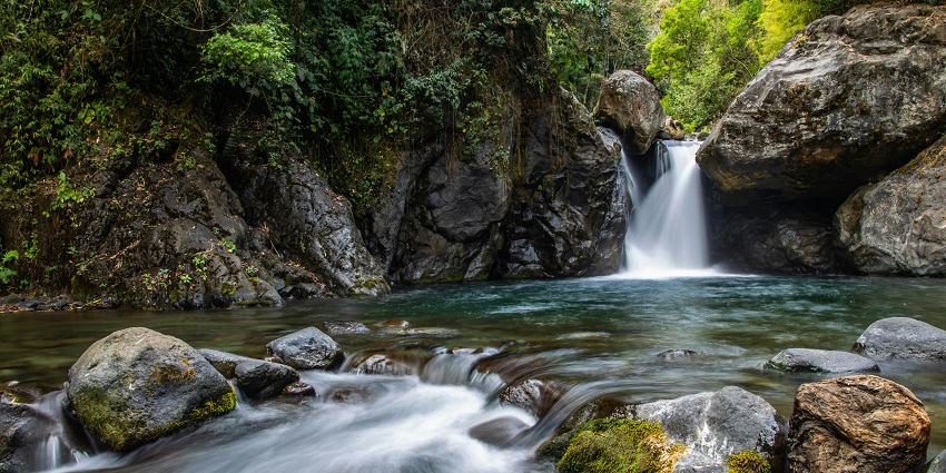 An image of one of the best waterfalls in Alaska flows through the forest
