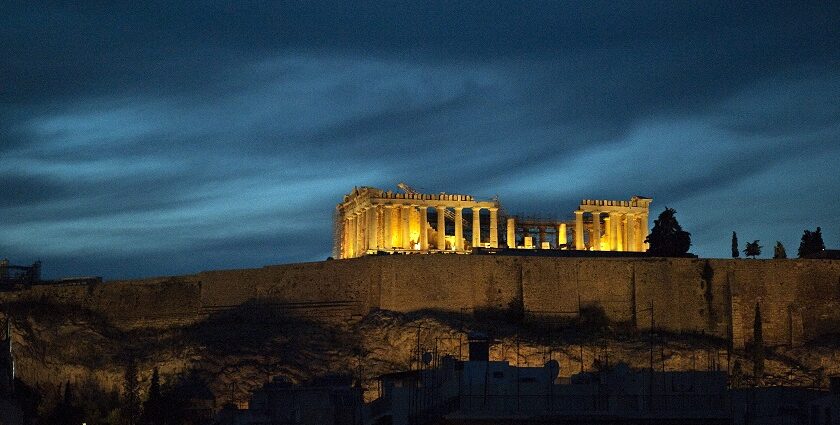 Acropolis Hill and Parthenon illuminated at night with ruined architecture and blue sky.