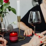 A couple holding hands while they are on a date with wine in glasses and a candle.