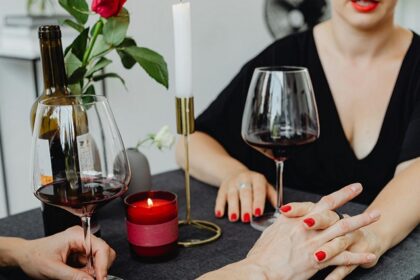 A couple holding hands while they are on a date with wine in glasses and a candle.