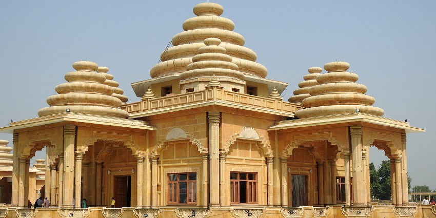 An image of Valmiki Ashram in Kanpur with many top structures and surrounded by water.