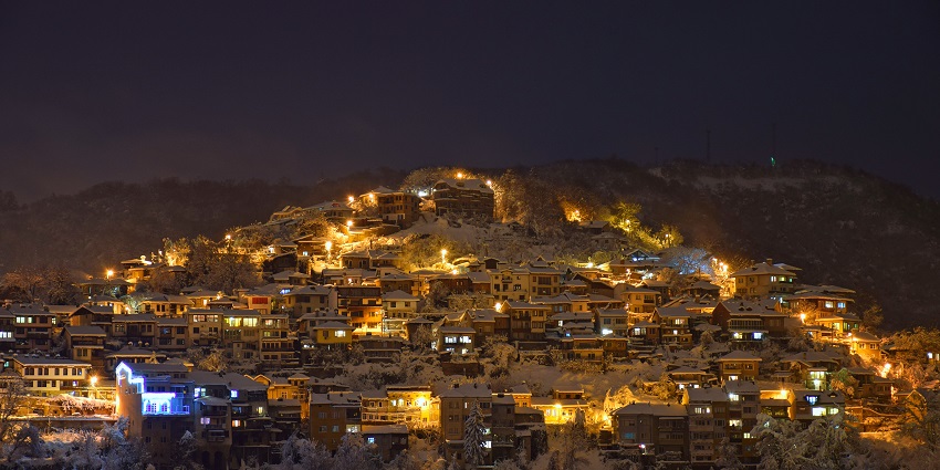 eliko Tarnovo city on a hill with well-lit buildings and houses, all covered in snow