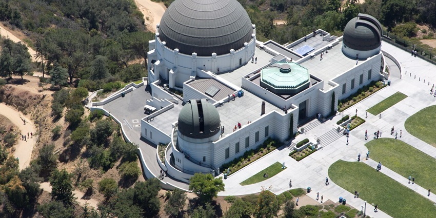 Griffith Observatory from above with two big telescopes on each side and people visiting