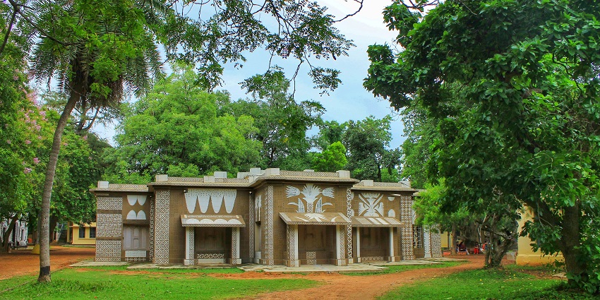 A picture of a building surrounded by a garden and lush greeenery