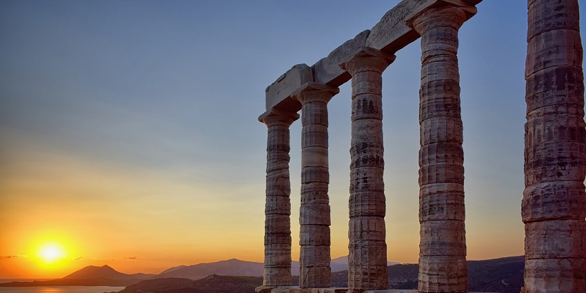 Temple of Poseidon at Cape Sounion with multiple stone pillars and sunset view and hills
