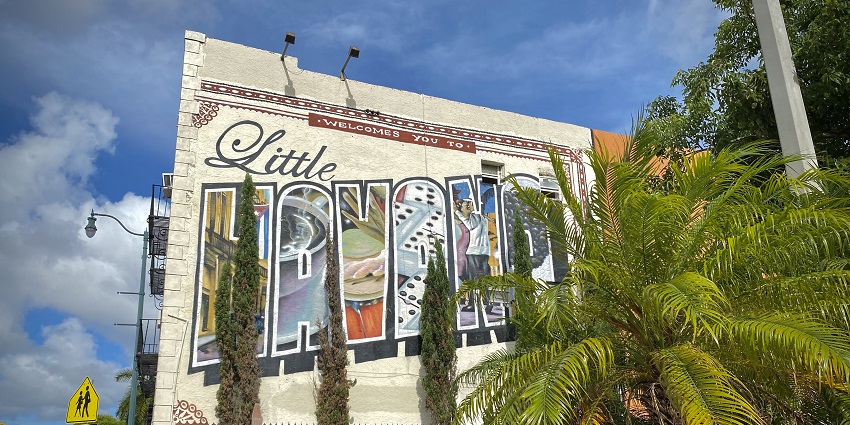 Little Havana painted on a wall with cars parked on the side of the street and street lamps.