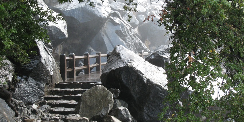 Footbridge below Wapama Falls, with water going down the cliffs in the background.
