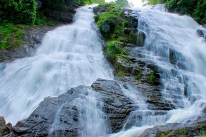 One of the waterfalls in California flows down rocks, surrounded by lush greenery.