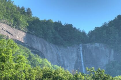 A serene view of Hickory Nut Falls in North Carolina, with the waterfall surrounded by green foliage.