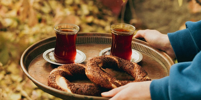 Image of a person carrying pretzels and drinks on a round plate in steel colour