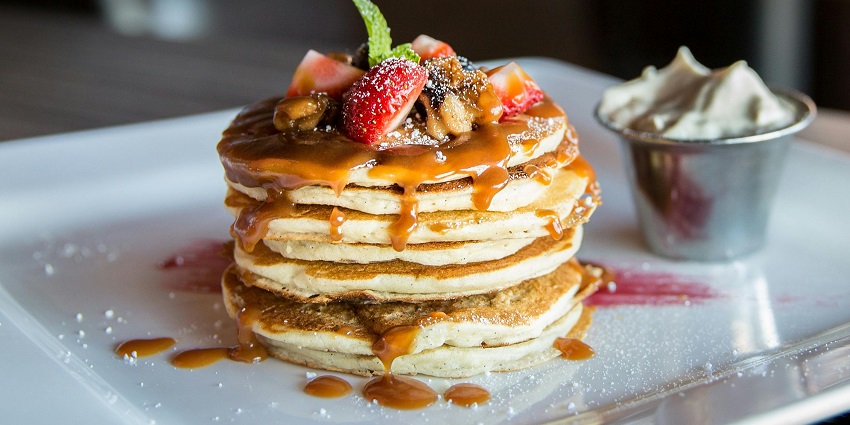 Close-up of a delicious pancake topped with sliced strawberries and syrup on a plate.