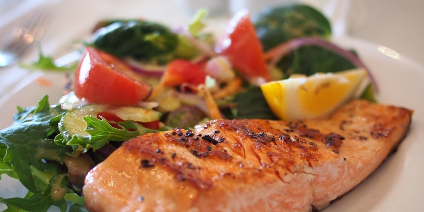 A grilled salmon fillet served with a side salad of mixed greens, tomatoes, and red onion.
