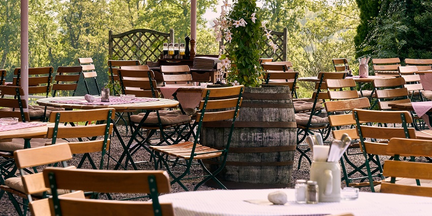 An outdoor seating area at a restaurant and chairs set up under a canopy of trees