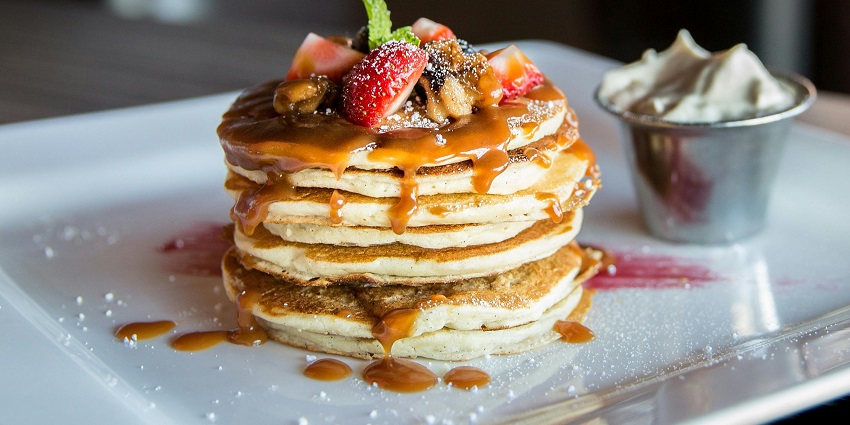 Image of tempting pancakes with strawberries on top and honey, served on a white plate