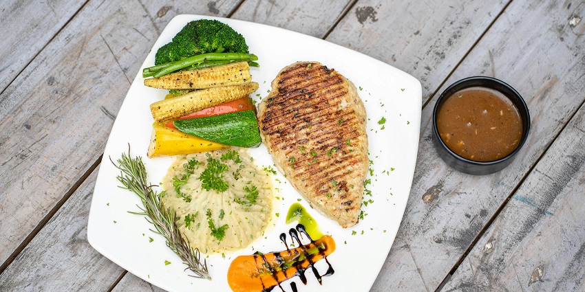 A photo of grilled fish steak served with vegetables and sauce on a white