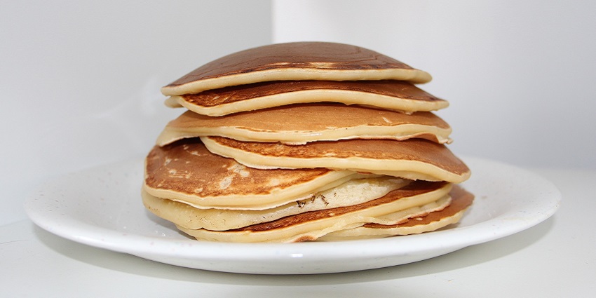 A stack of golden-brown pancakes topped with melting butter, served on a white plate
