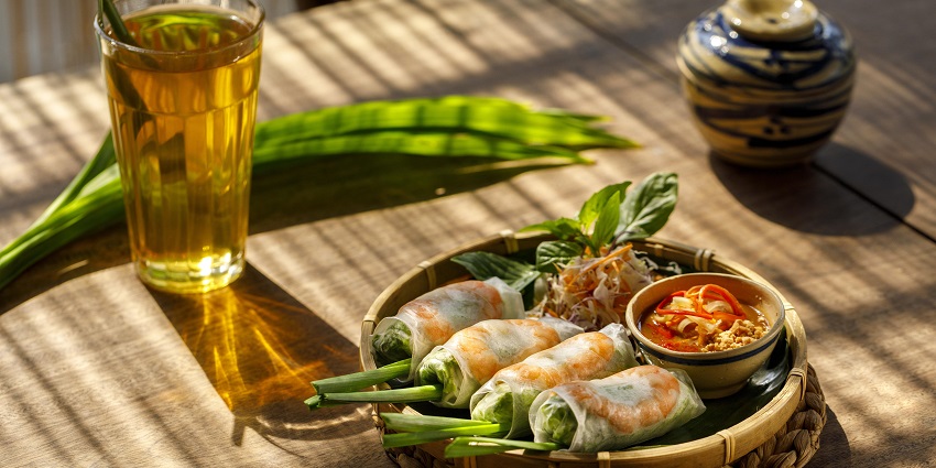 An image of spring rolls filled with fresh vegetables and shrimp, served with sauce