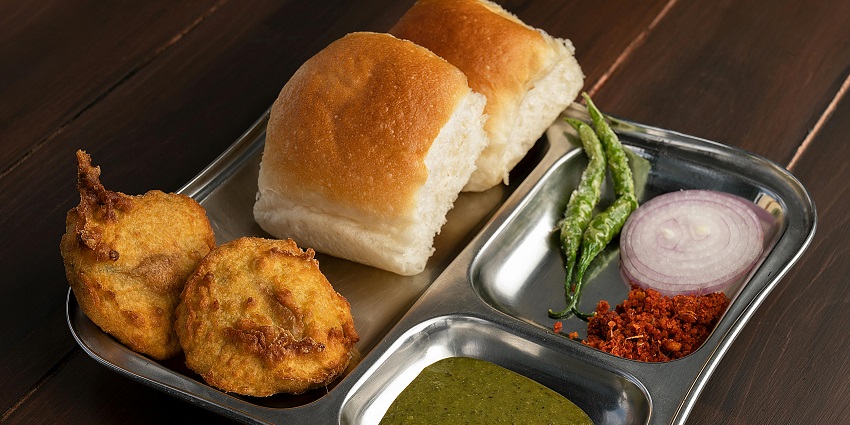 Image of Vada pav plate served on a steel plate with pakoda, chutney on the side