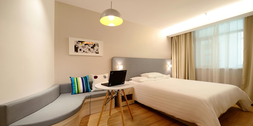 An image of a black laptop placed on a wooden table, with a blurred background in a hotel.