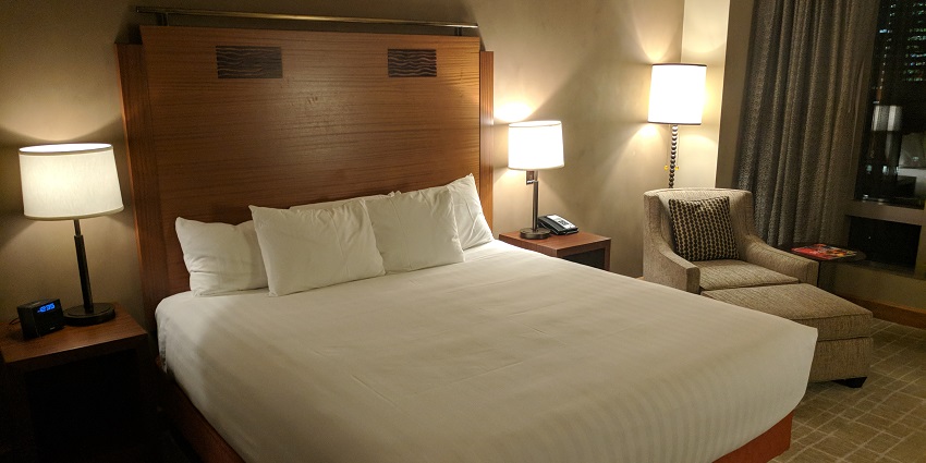 A hotel room with a plush bed, warm lighting, modern decor, and a scenic window view.