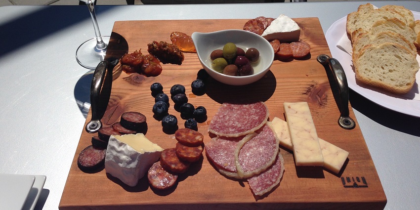 A glass of wine served with cranberries, cheese, toasted bread and a charcuterie platter.