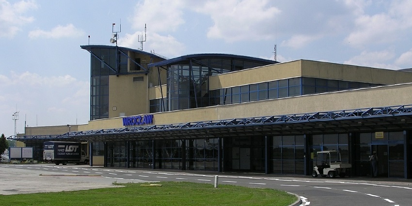 Building of Wrocław Copernicus Airport with a driveway, signage, and a luggage carrier