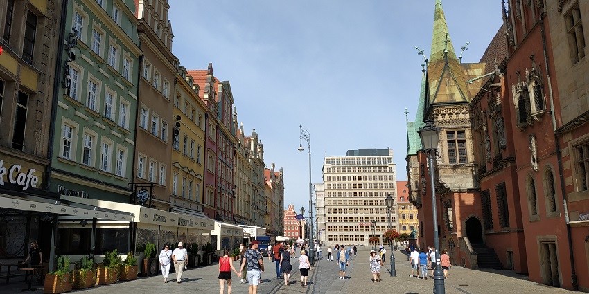 Street in Wrocław with people walking while holding hands, tall buildings, cafes and shops