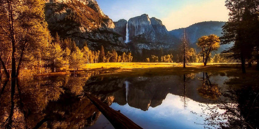 A towering granite mountain is located behind the serene nature of Yosemite National Park.