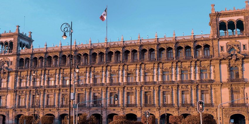 The famous square of Mexico City, which has a Mexican flag in the centre has people around.