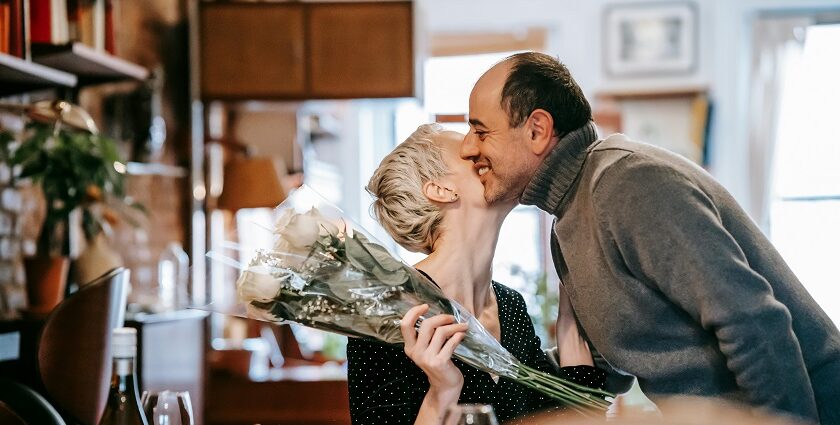 A couple kissing while the woman holding a flower bouquet with a wine bottle and a glass