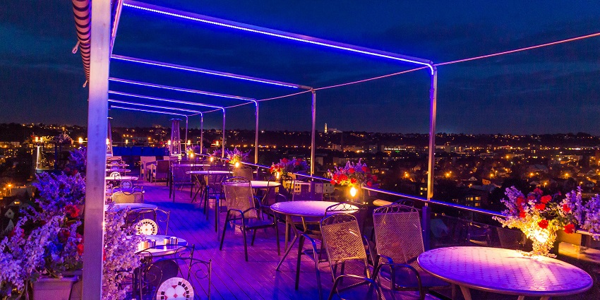 Rooftop club in purple lighting with restaurant chairs and tables set near the boundary